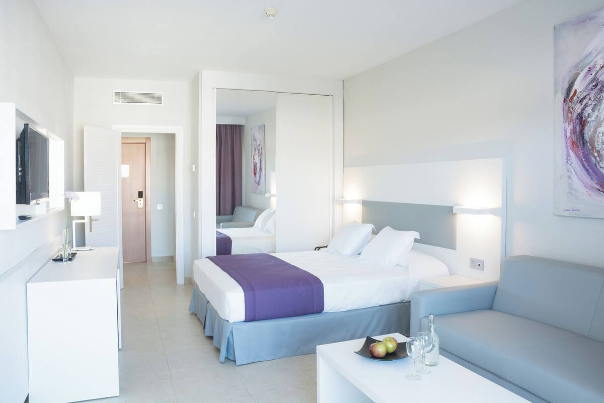 A modern hotel room with a bed, a sofa, a desk, and a TV.