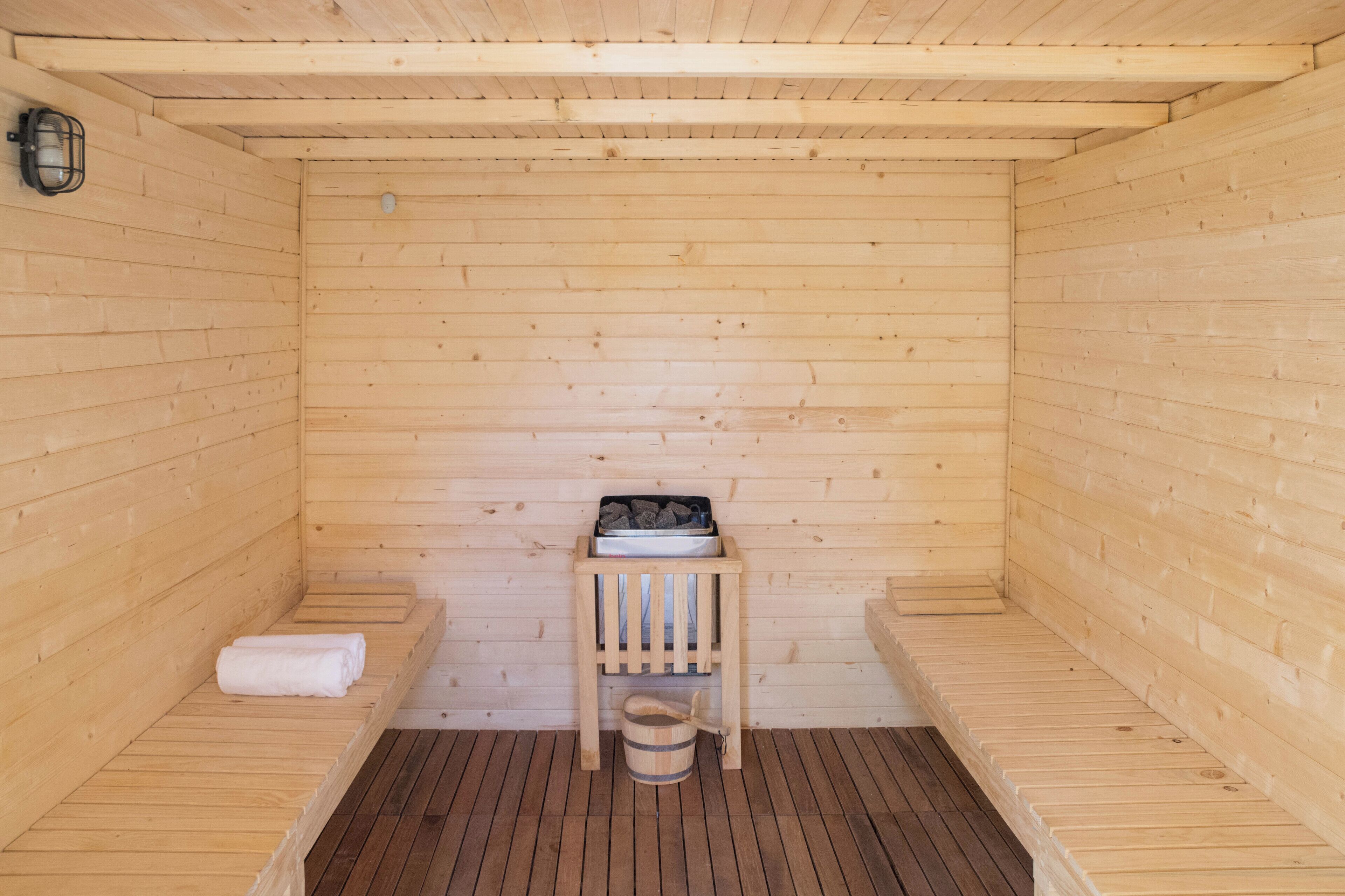 A wooden sauna with benches, a small table with a bucket, and a towel on the floor.