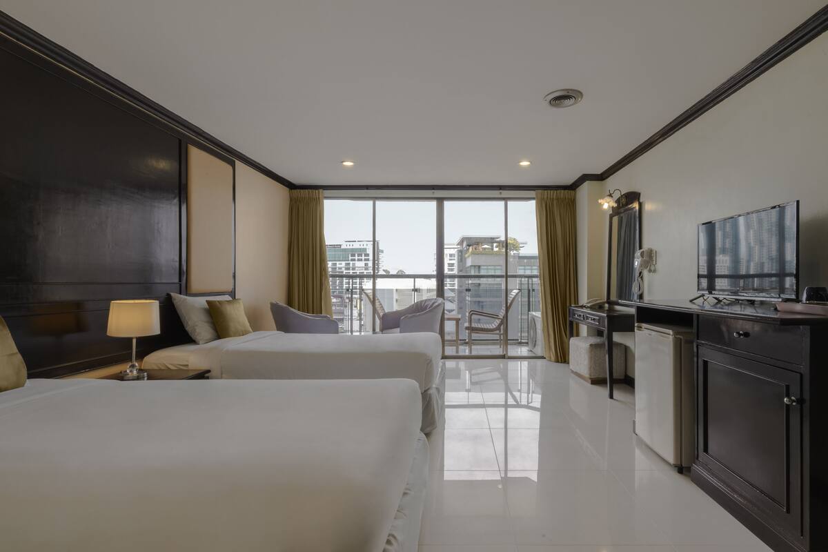 A hotel room with two beds, a desk, a television, and a balcony with a city view.
