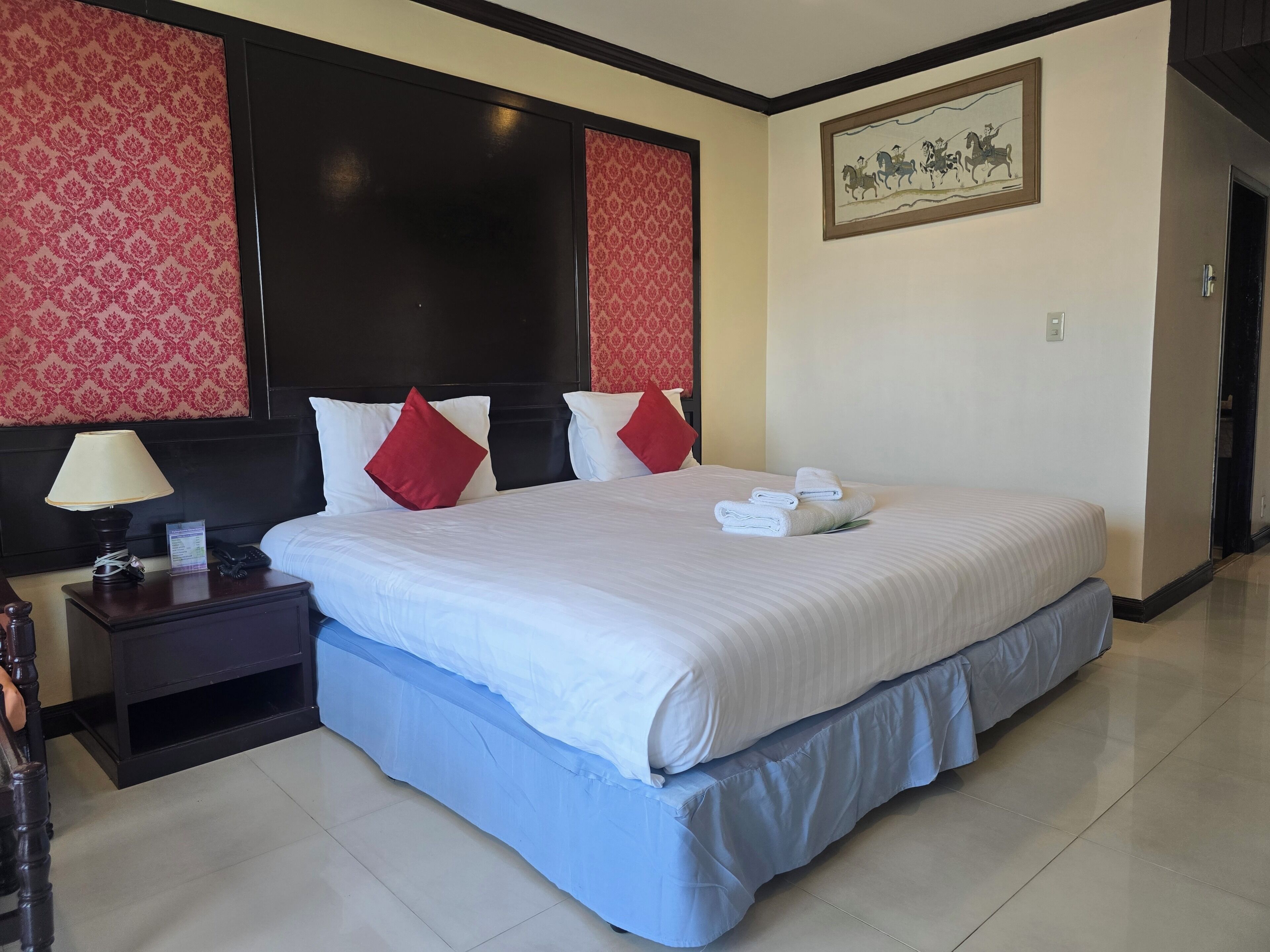A hotel room with a large bed, a nightstand with a lamp, and a framed picture on the wall.
