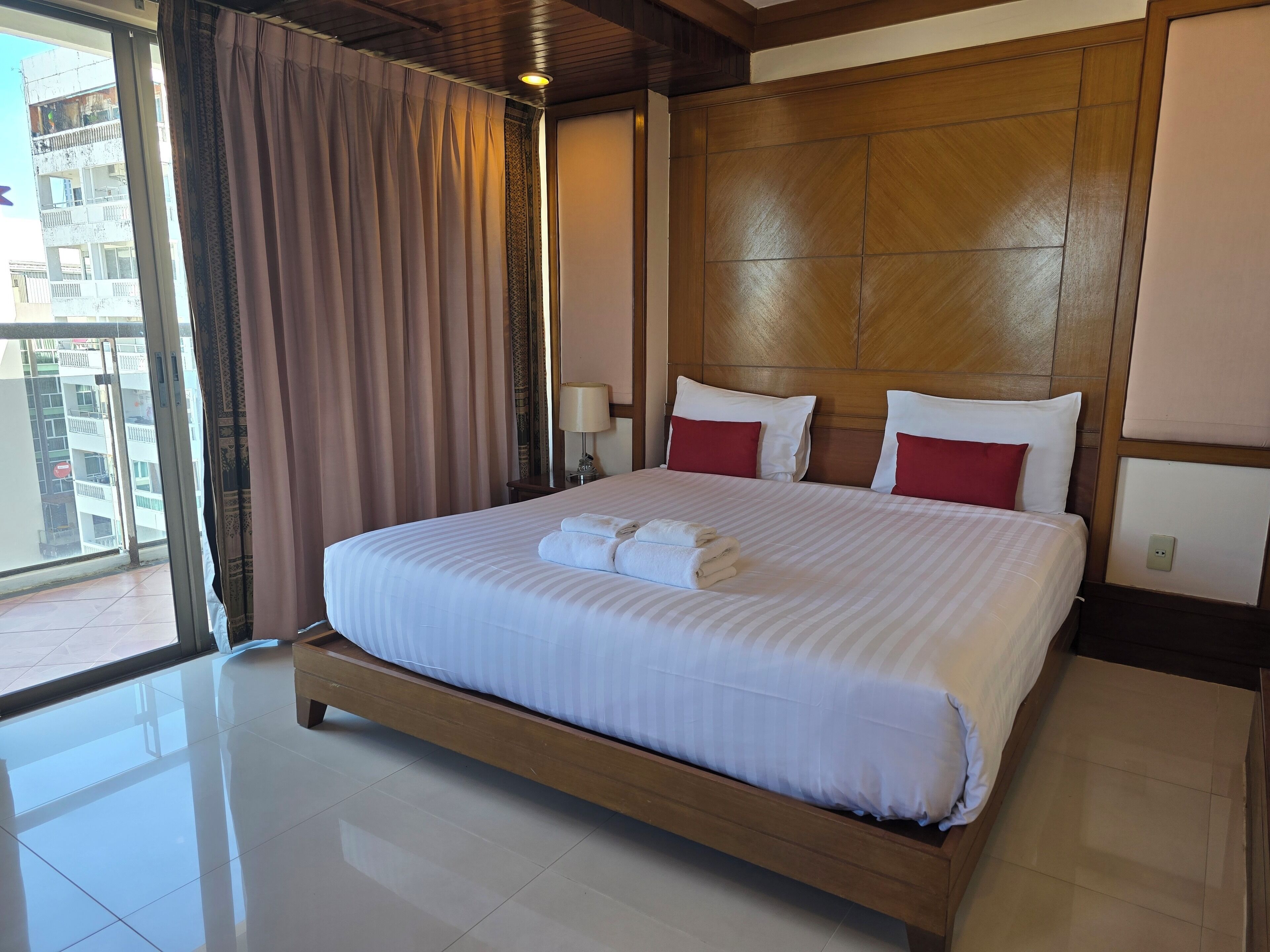 A hotel room with a large bed, wooden headboard, and a view of a building through a large window.