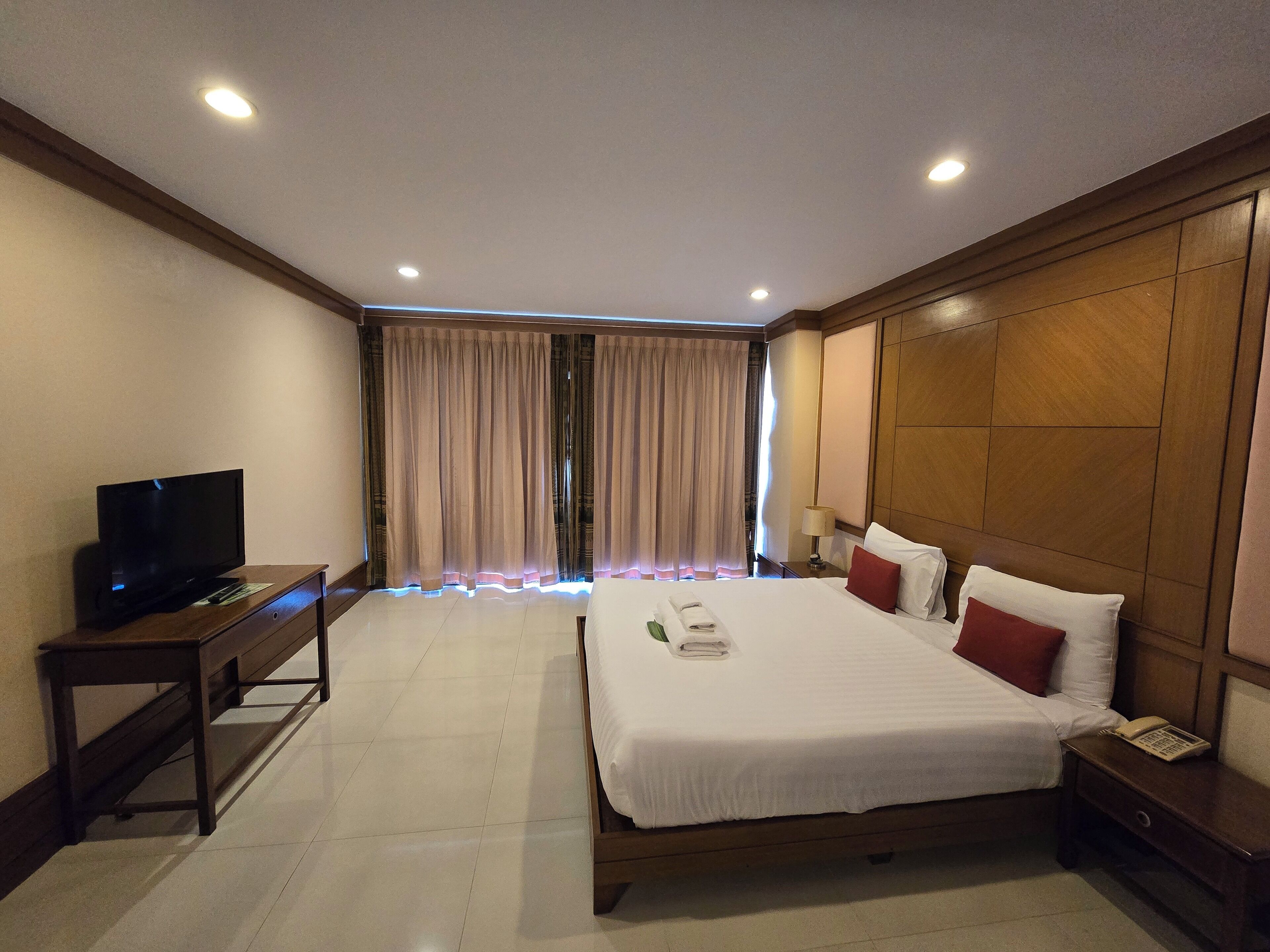 A hotel room with a bed, bedside table, TV, and curtains.