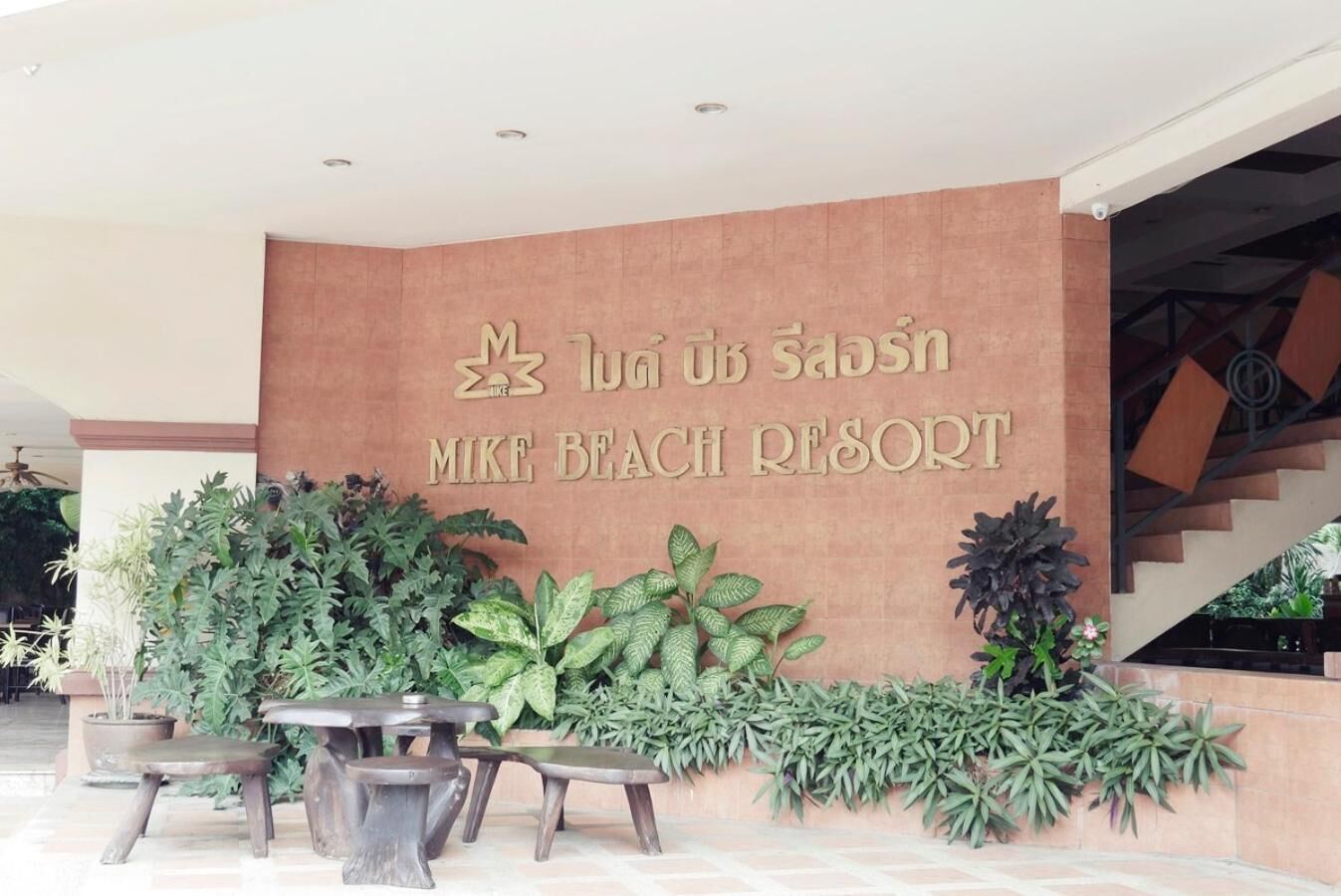 Un espace d’accueil au Mike Beach Resort, avec un panneau indicateur, des plantes en pot et un escalier.