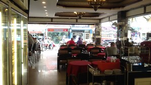 An indoor restaurant with tables covered in red tablecloths, a ceiling fan, and a sign for 'We're DRUGS' visible outside. - Katesiree House (Pattaya)