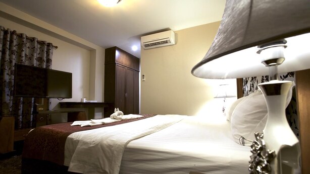 A hotel room with a bed, a television, an air conditioning unit, a lamp, and a decorative vase. - Katesiree House (Pattaya)