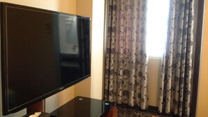 A room with a flat-screen TV on a stand, floral curtains, and a window with a view. - Katesiree House (Pattaya)