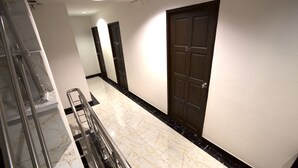 A hotel corridor with marble flooring, a metal handrail, and dark wooden doors. - Katesiree House (Pattaya)