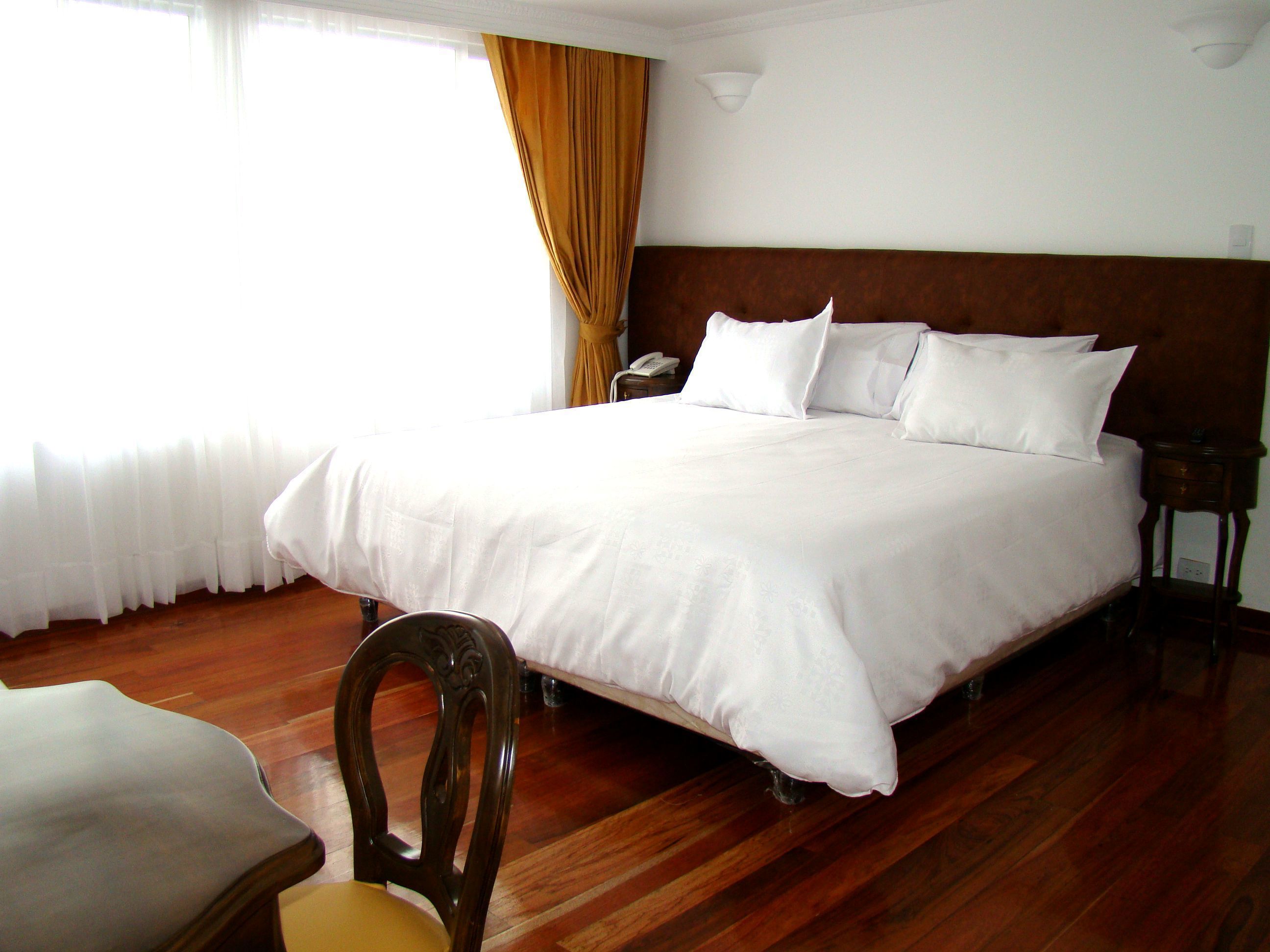 Une chambre d’hôtel avec un grand lit, un plancher en bois et une chaise.
