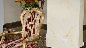 A gold-framed chair with a patterned cushion and a vase of tropical flowers on a marble floor. - Hotel Boutique Feria Internacional (Bogotá)
