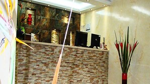 A reception area with a stone wall, a reception desk, and a vase with red flowers. - Hotel Boutique Feria Internacional (Bogotá)