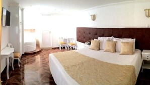 A hotel room with a large bed, a desk, two chairs, a TV, and a window with curtains. - Hotel Boutique Feria Internacional (Bogotá)