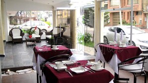 A restaurant with tables set for dining, outdoor seating, and a view of parked cars and buildings. - Hotel Boutique Feria Internacional (Bogotá)