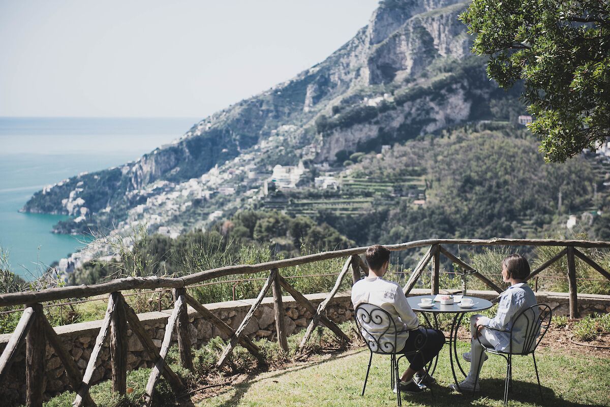 Two people seated at a table with a view of a coastal landscape and mountains.