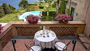 Una terraza con una mesa preparada para el té, con vistas a una piscina y un jardín lleno de flores rosadas.