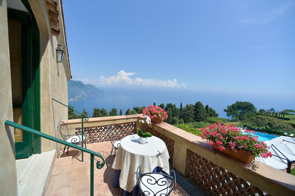 Un balcon avec une table et des chaises, offrant une vue panoramique sur la mer et la verdure.