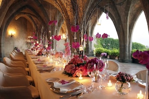 Una larga mesa de comedor dispuesta para un evento formal, con velas y centros de mesa florales.