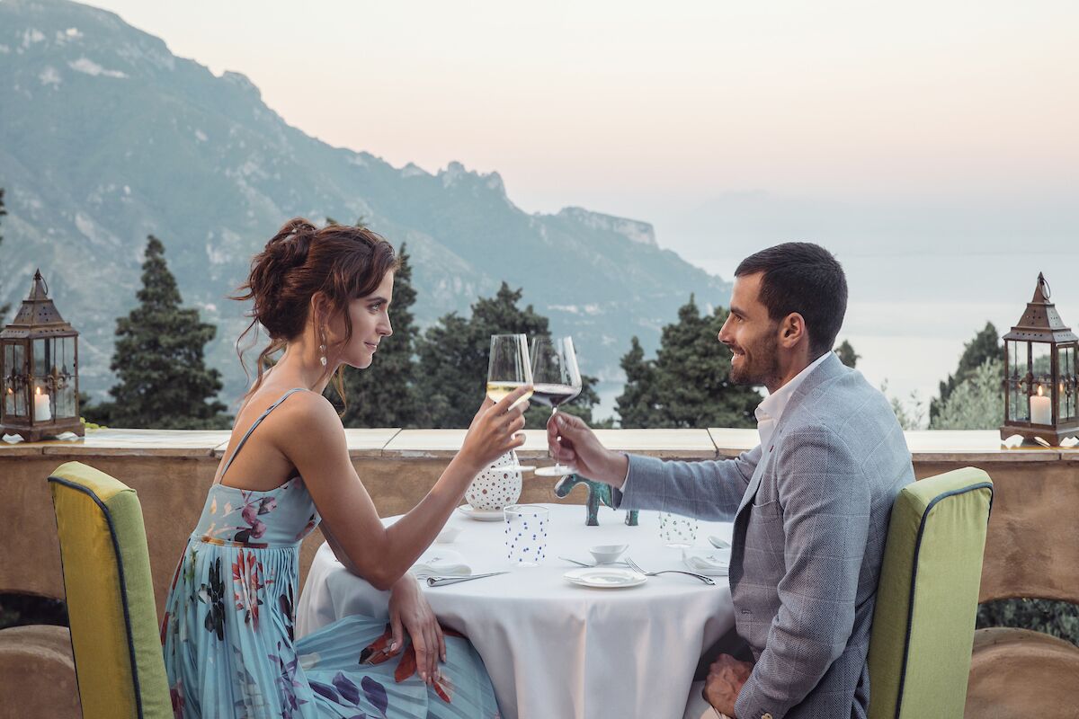 A couple toasting at a table with a mountain view in the background.
