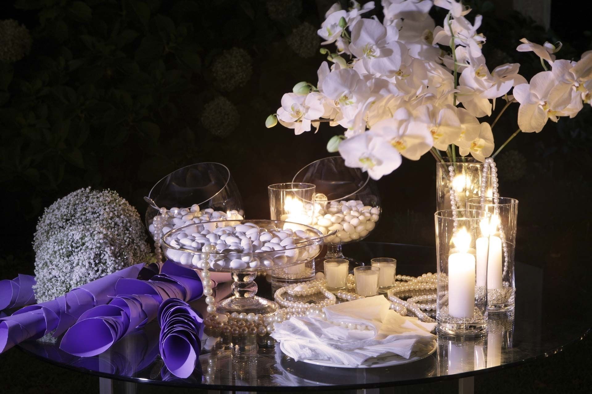 Una mesa con candelabros de vidrio, velas blancas y adornos de perlas.