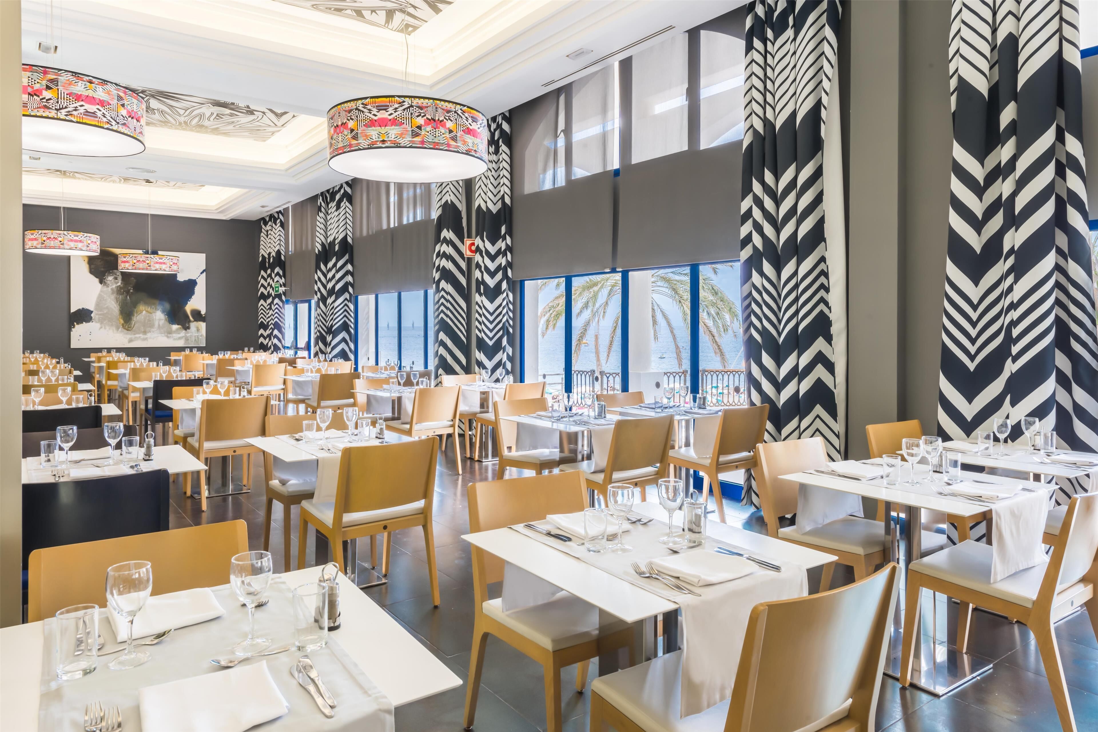 A modern restaurant with multiple dining tables, chairs, and hanging decorative lamps.
