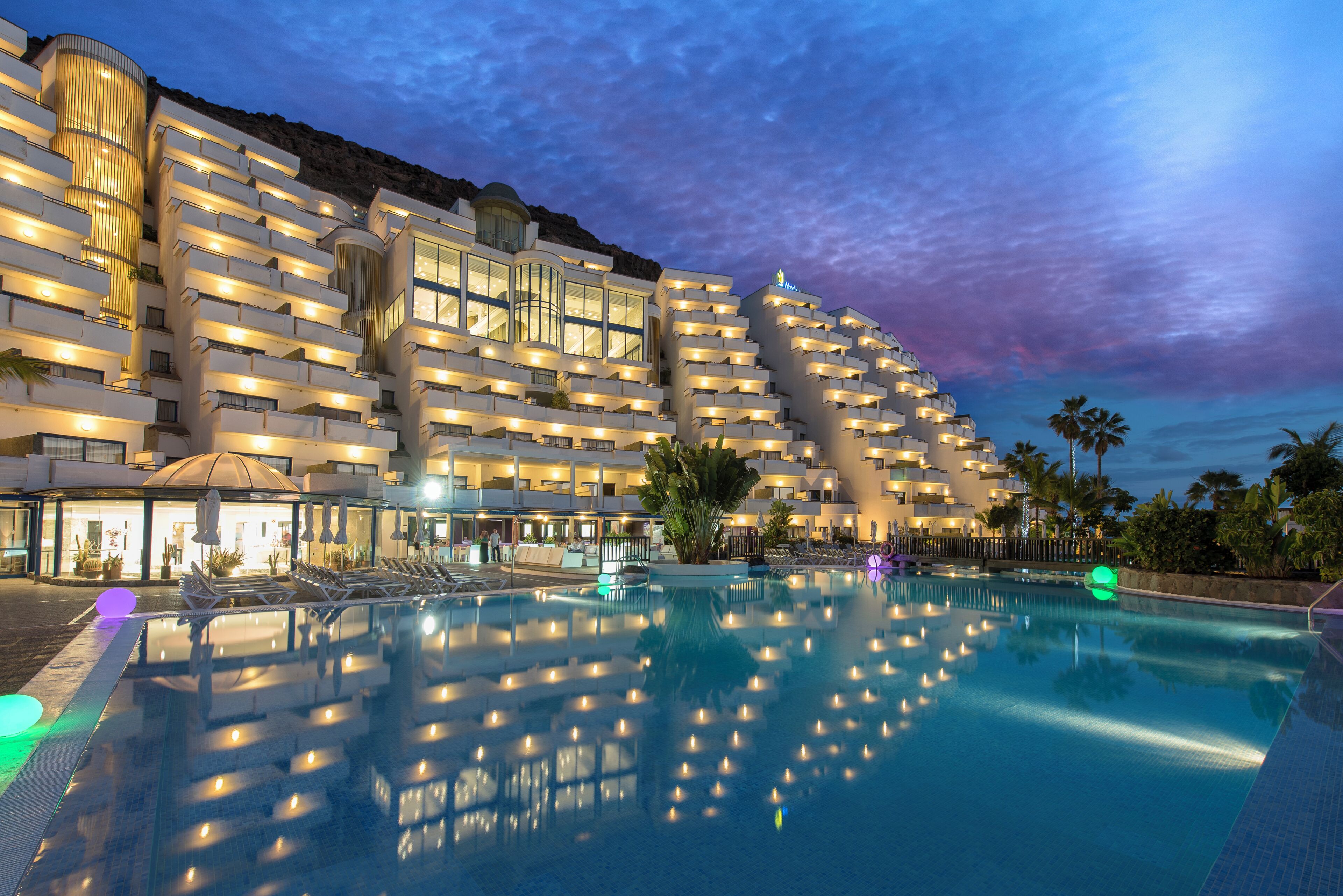 A hotel with multiple balconies, a swimming pool, and a view of the sky.