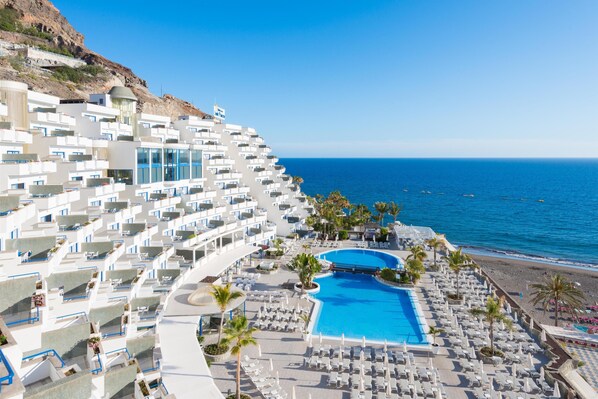 A resort with a large pool, multiple balconies, and a beach view.