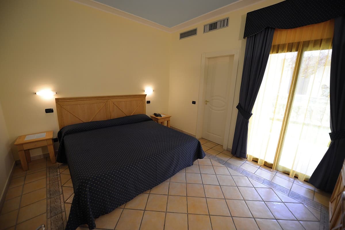 A bedroom with a bed, bedside tables, a nightstand, a door, and a window with curtains.