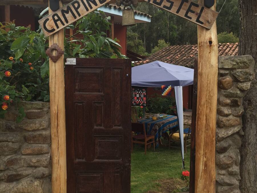 A wooden archway with "CAMPING HOSTEL" signage, a closed wooden door, and a stone wall.