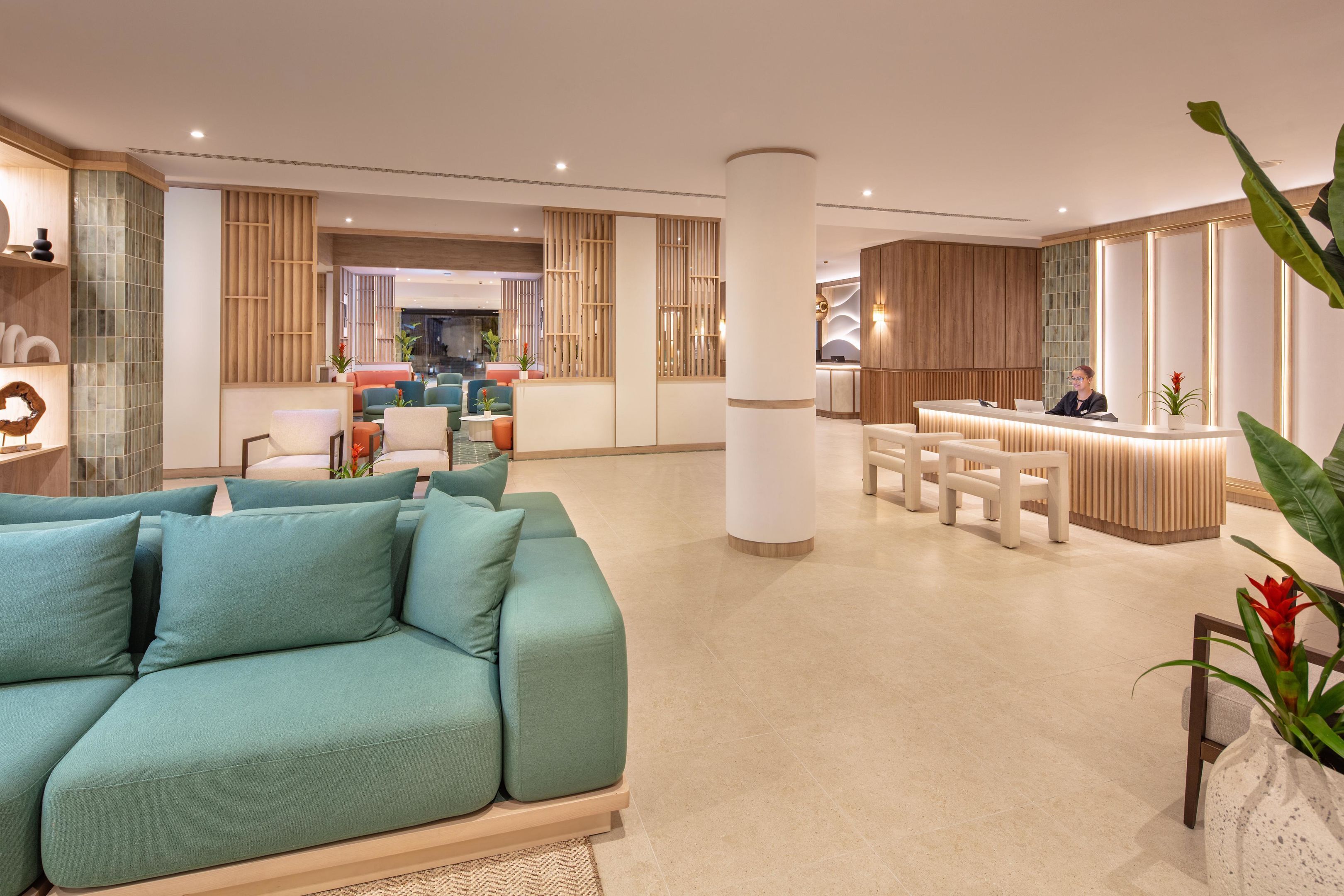 Un moderno vestíbulo de hotel con mostrador de recepción, zona de estar y un amplio sofá verde.