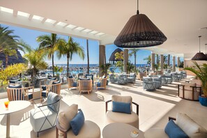 Amplia zona de estar al aire libre con diversas opciones de asientos, piscina y vistas a la playa y al océano.