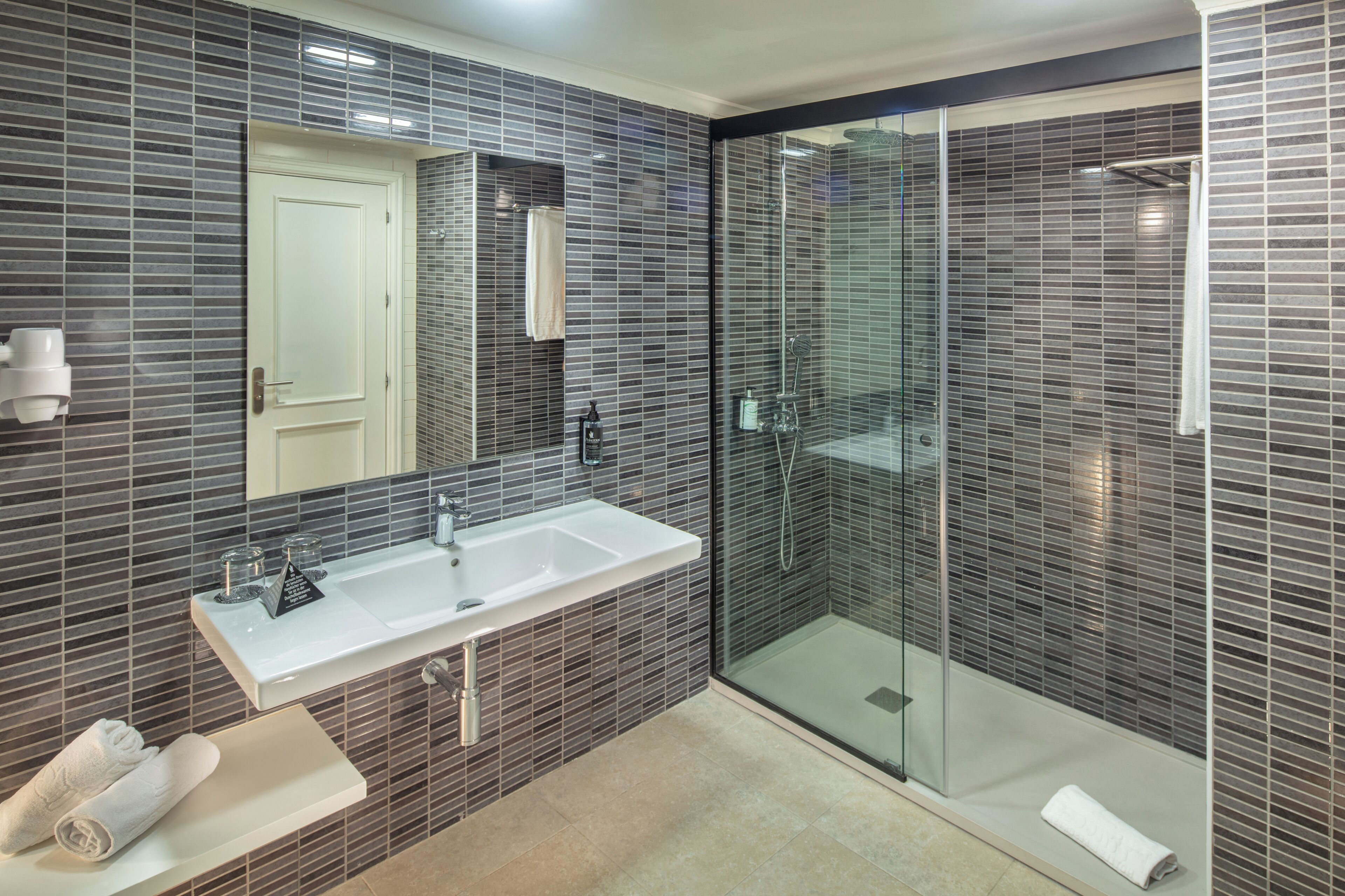 A modern bathroom with a large sink, mirror, and walk-in shower.