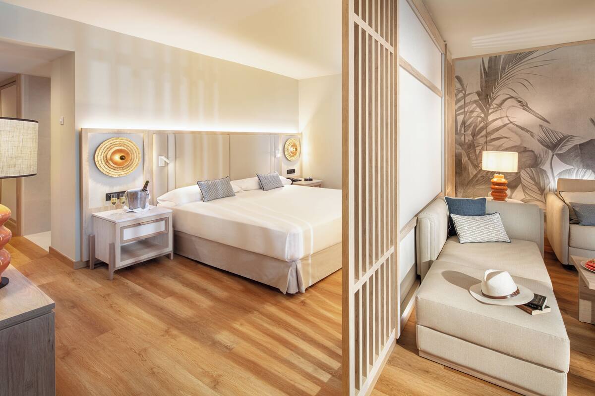 A hotel room with a large bed, a sofa, a nightstand, and a lamp.