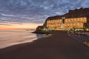 Un hotel con un edificio grande que domina una playa, destacando un acantilado y vistas al mar.