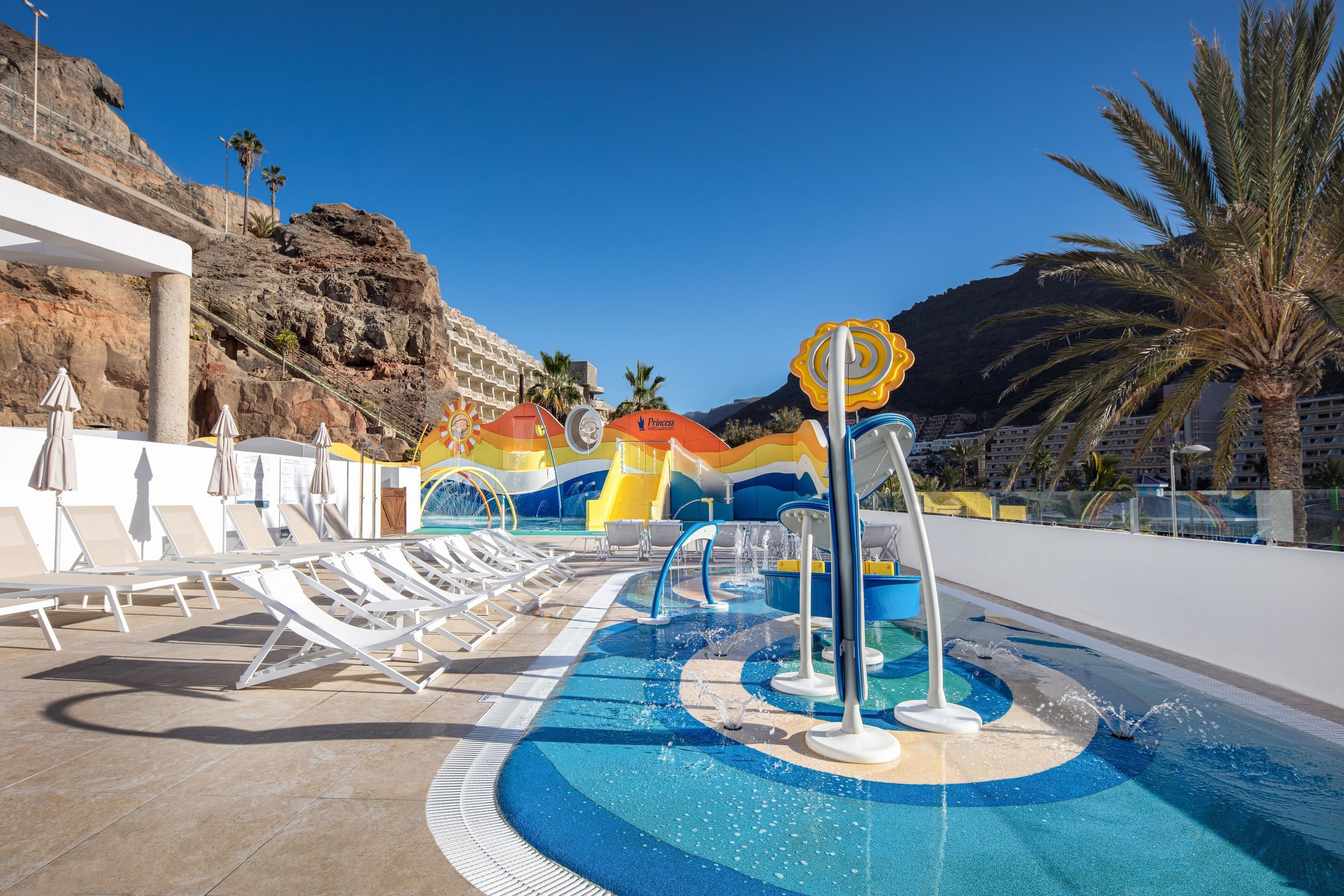 A pool area with lounge chairs, a water feature, and a mountain backdrop.