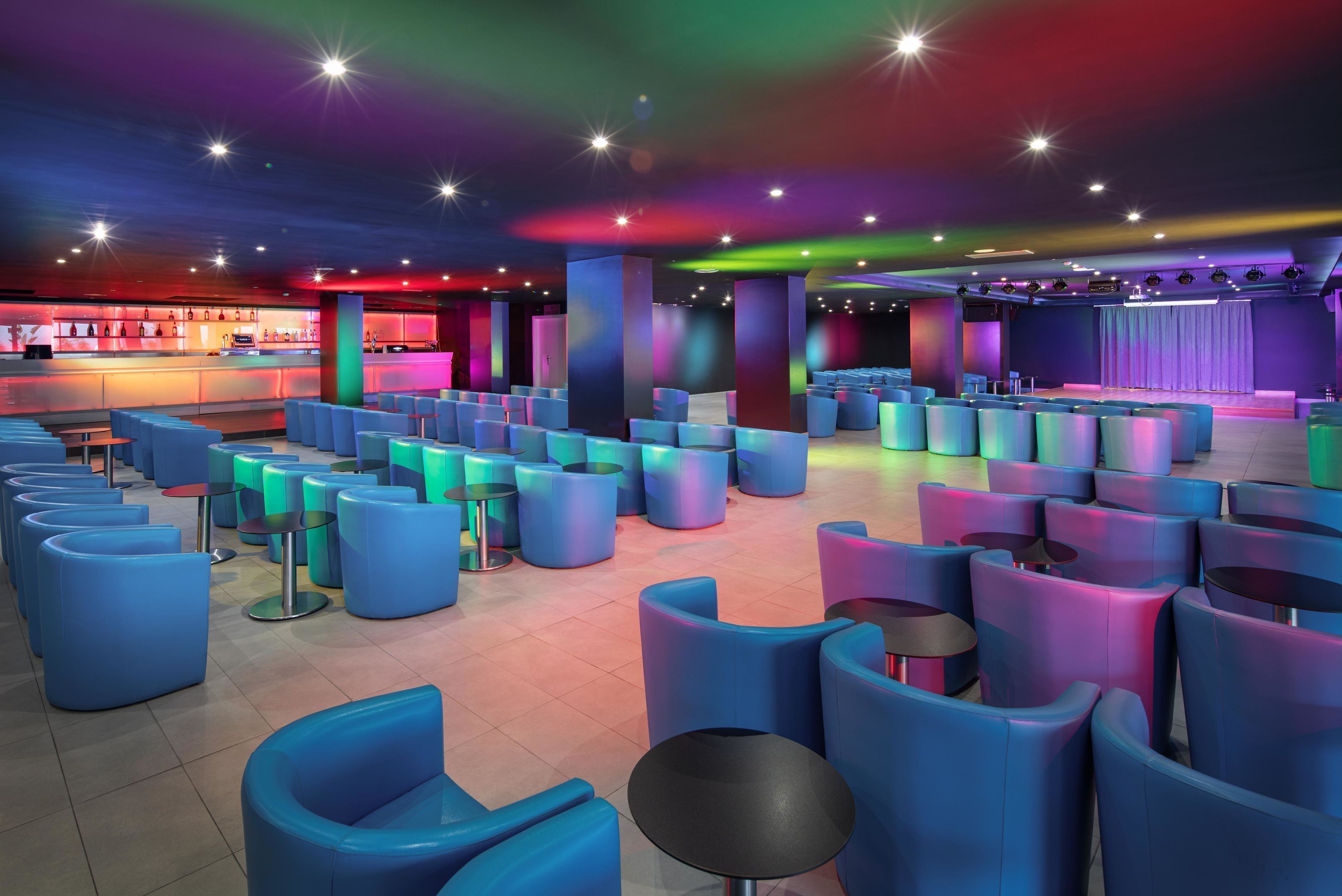 Ein großzügiger Loungesbereich mit blauen Sitzreihen und einer Bar im Hintergrund.