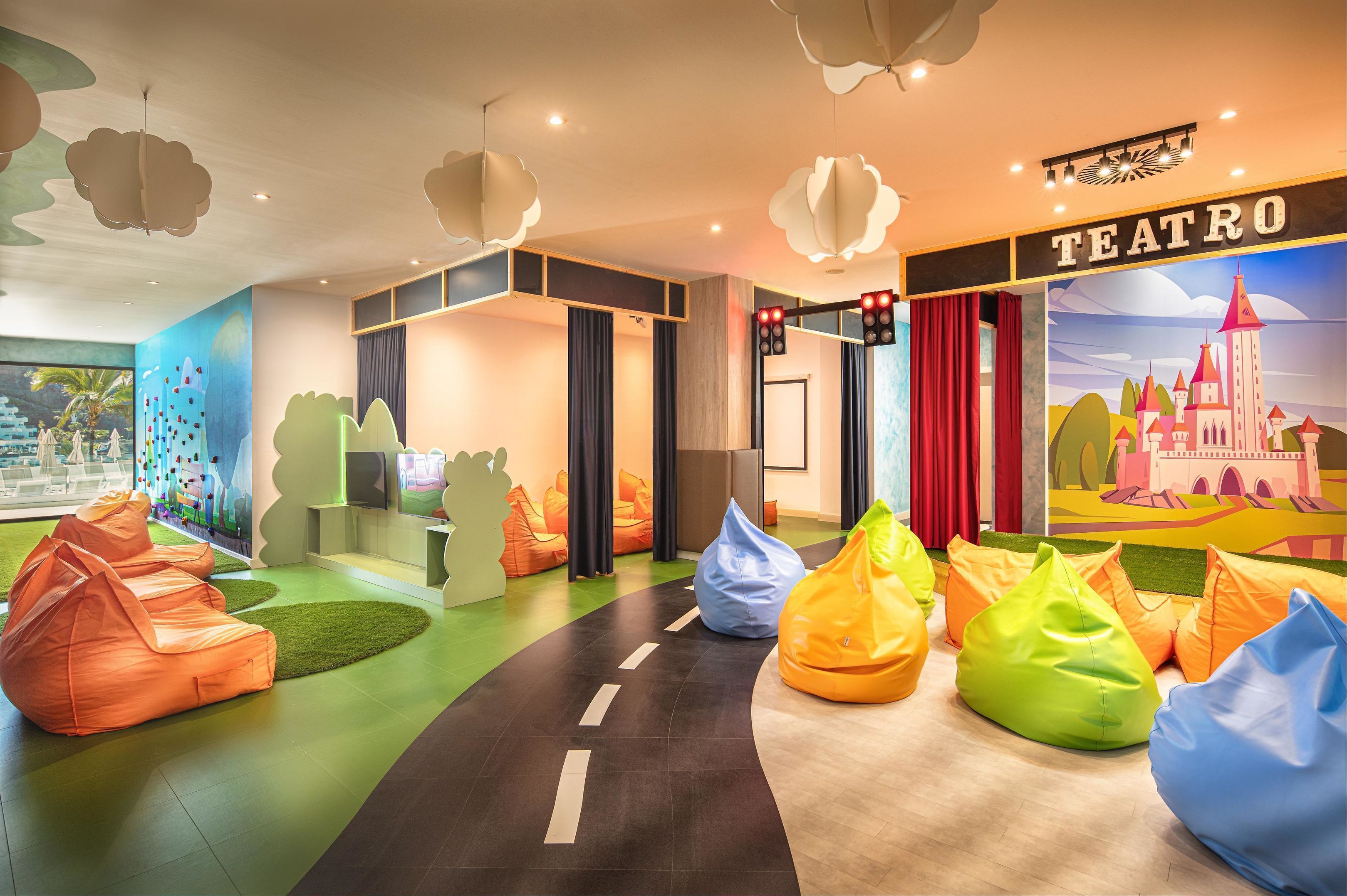 Un intérieur coloré avec des fauteuils en forme de sac de haricots, une fresque murale et une enseigne sur laquelle on peut lire « TEATRO ».