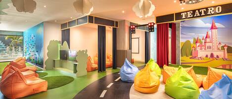 Un intérieur coloré avec des fauteuils en forme de sac de haricots, une fresque murale et une enseigne sur laquelle on peut lire « TEATRO ».