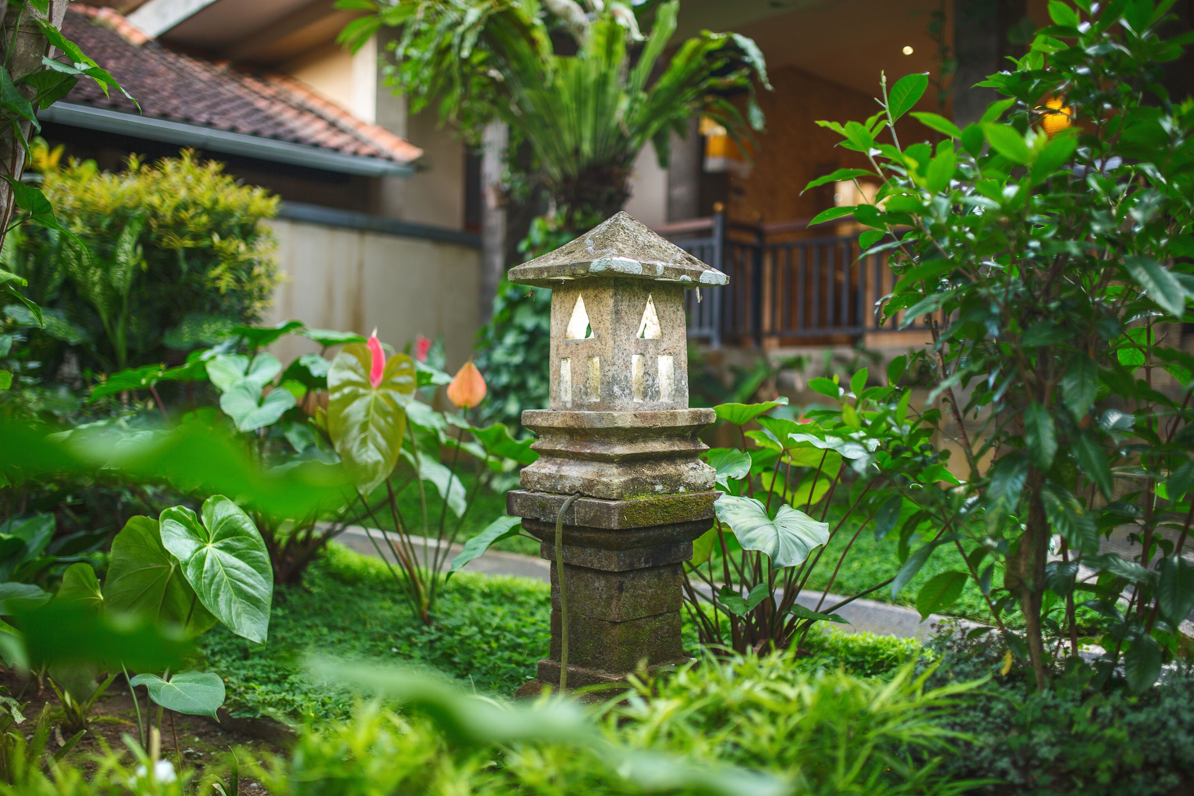A stone lantern in a lush garden with various plants and a building in the background.