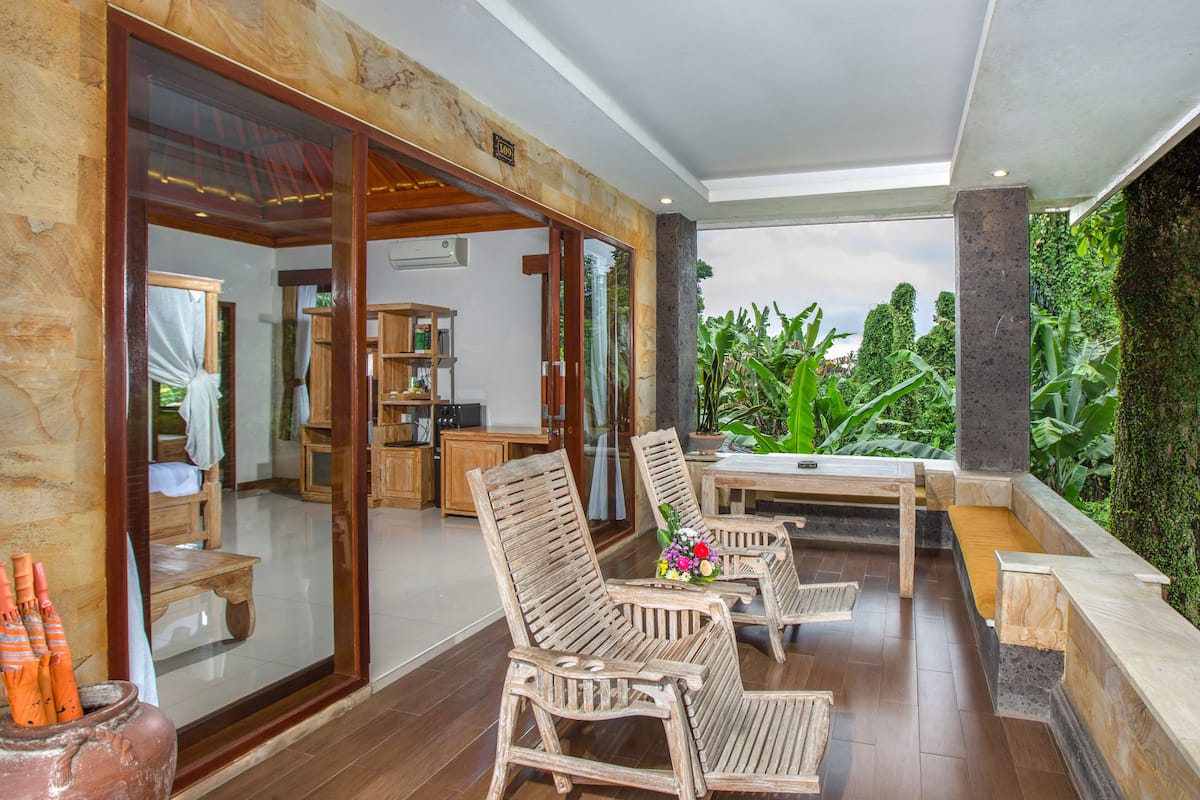 Une terrasse en bois avec des meubles d’extérieur, une vue sur une végétation luxuriante et une porte vitrée donnant sur un espace intérieur.