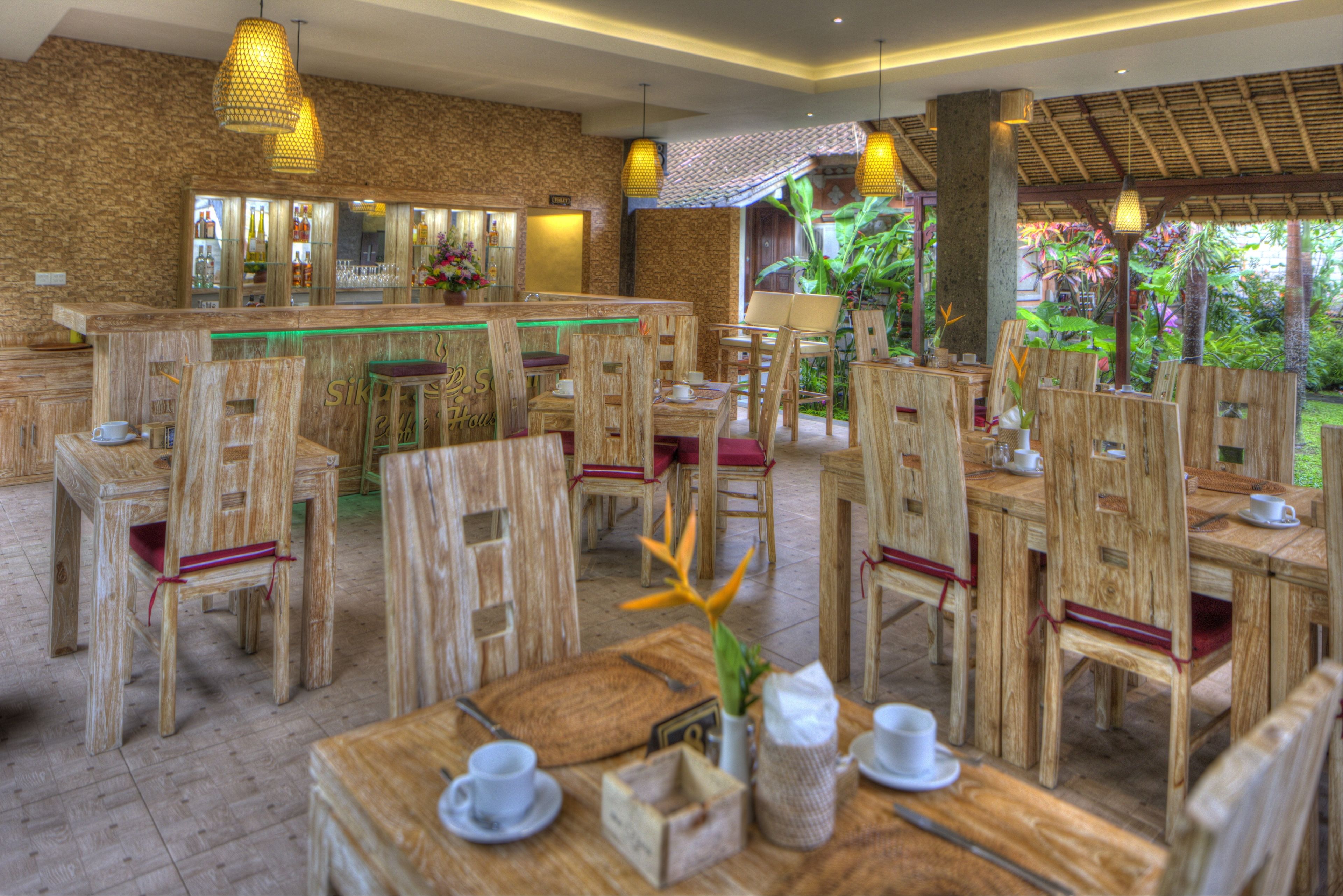 A wooden-furnished dining area with tables and chairs, a bar area, and a view of greenery outside.
