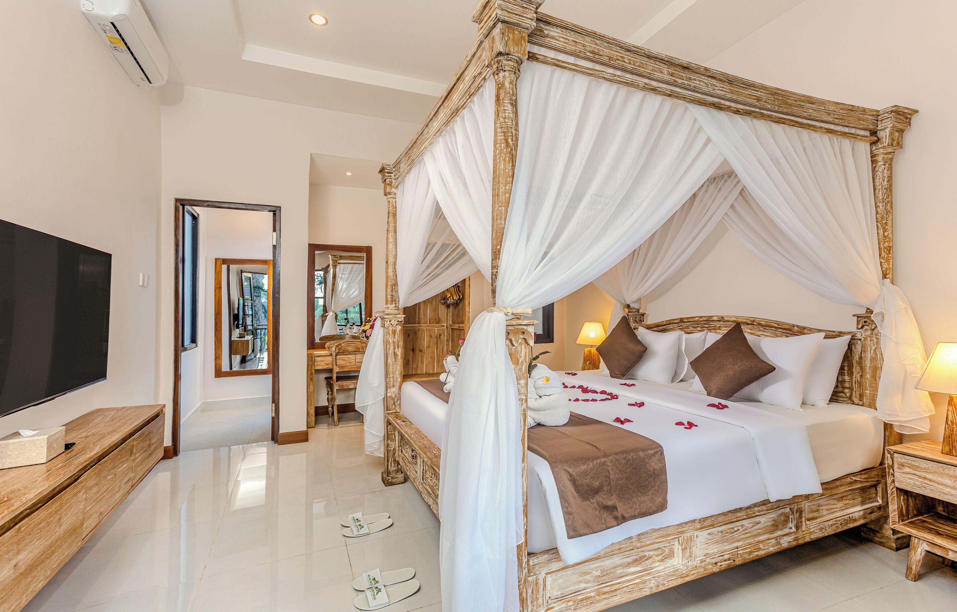 A four-poster bed with white drapes, a television, and a wooden nightstand.
