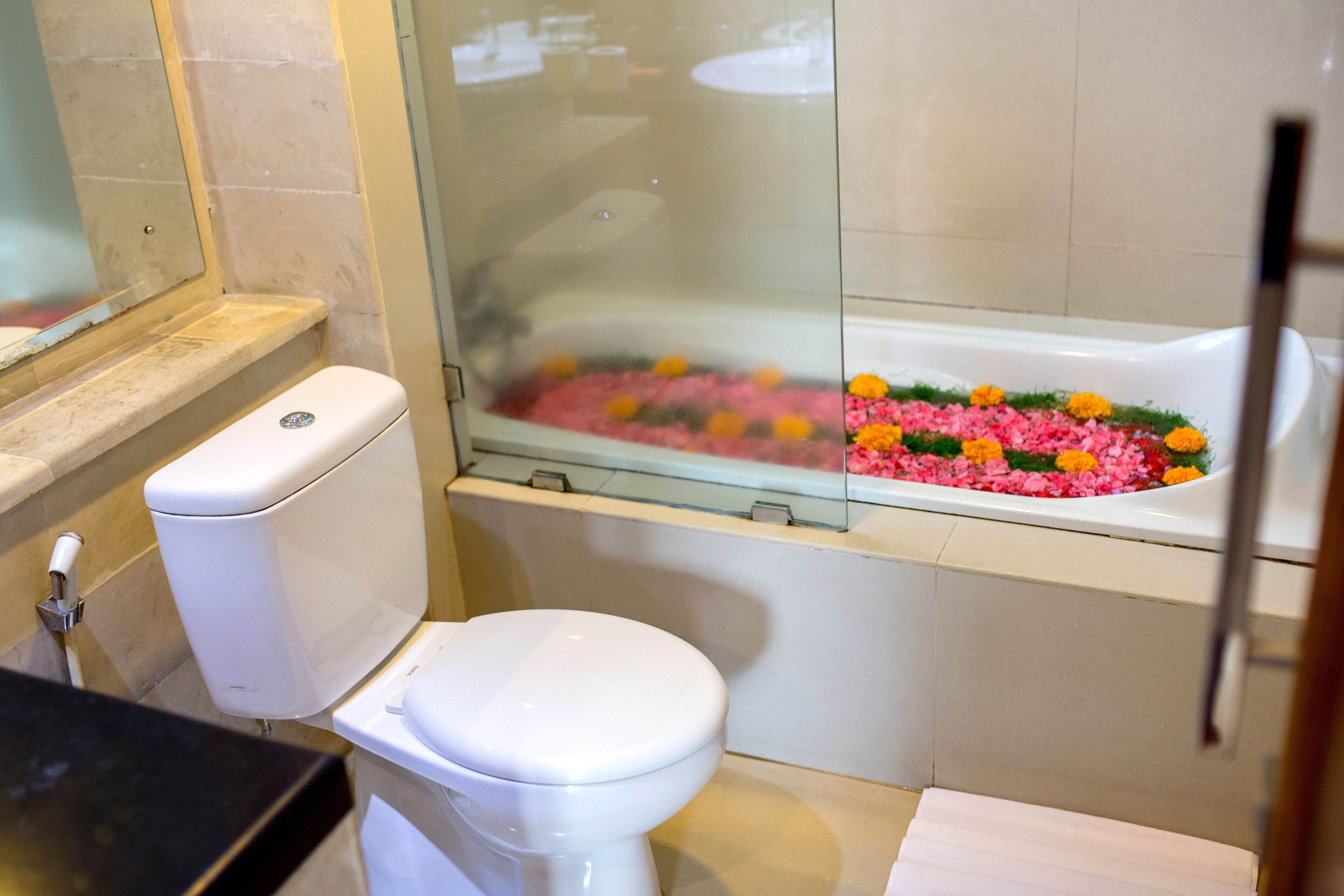 A bathroom with a toilet, a glass-enclosed shower, and a bathtub filled with flower petals.