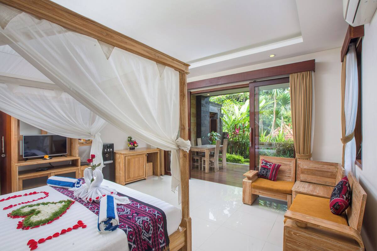 Quarto de hotel com cama, televisão, escrivaninha e área de estar com vista para o jardim.