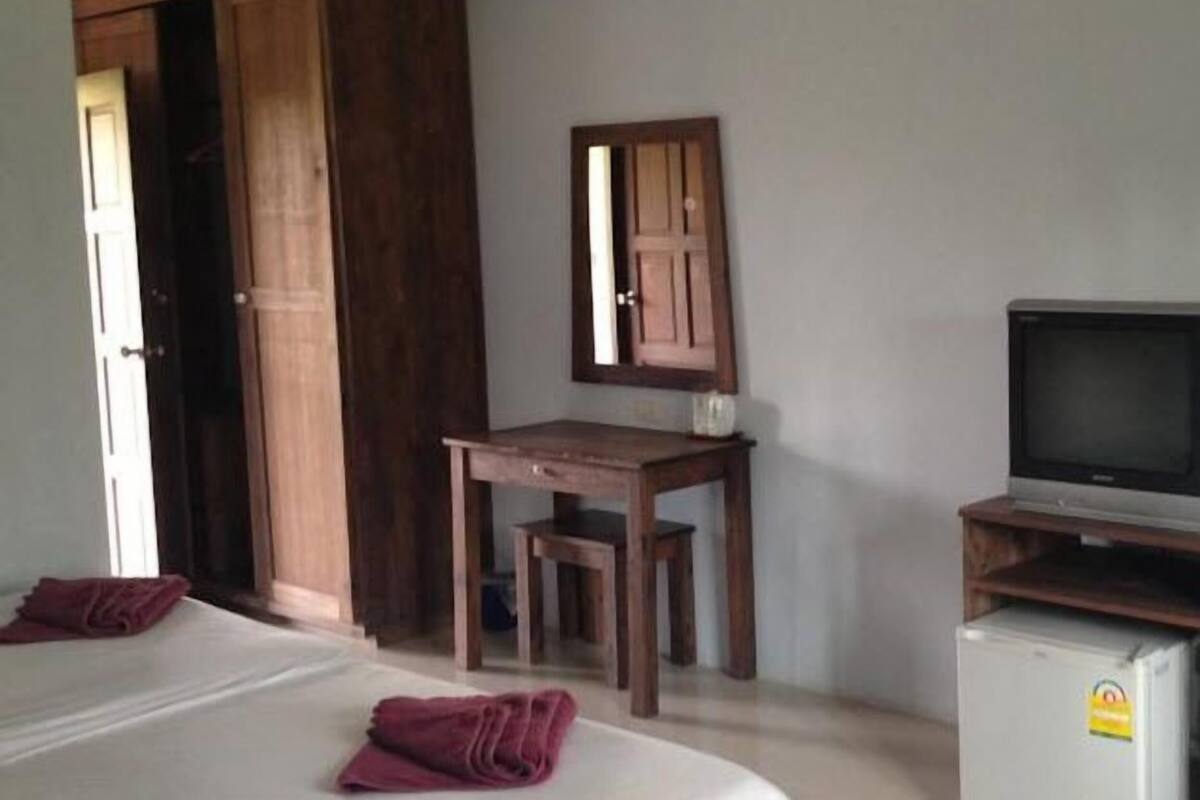 A hotel room with a bed, a desk with a chair, a television, and a refrigerator.
