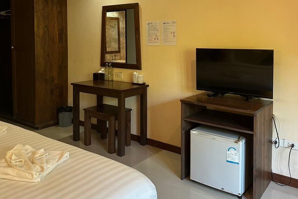 A hotel room with a bed, a desk with a mirror, a television, and a mini-fridge.