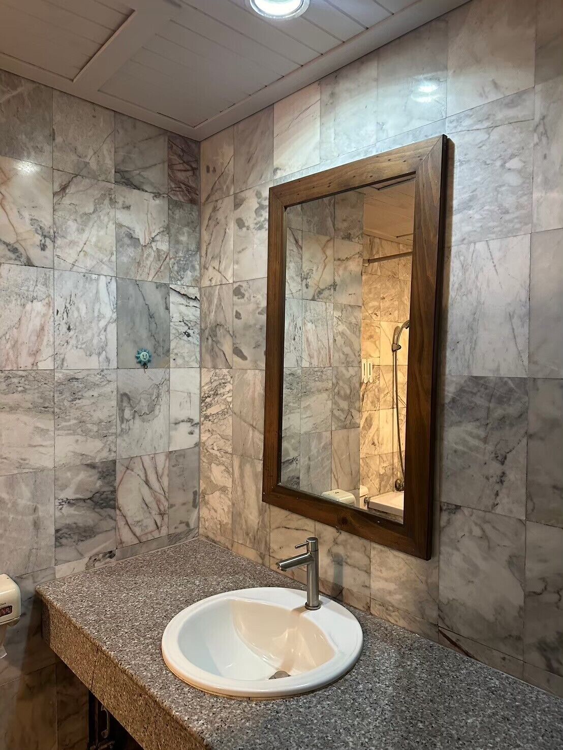 A bathroom with a marble wall, a wooden-framed mirror, and a granite countertop with a sink.