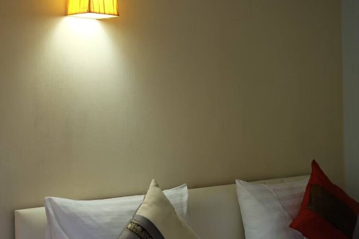 A hotel room with a bed, white bedding, and a wall-mounted lamp.