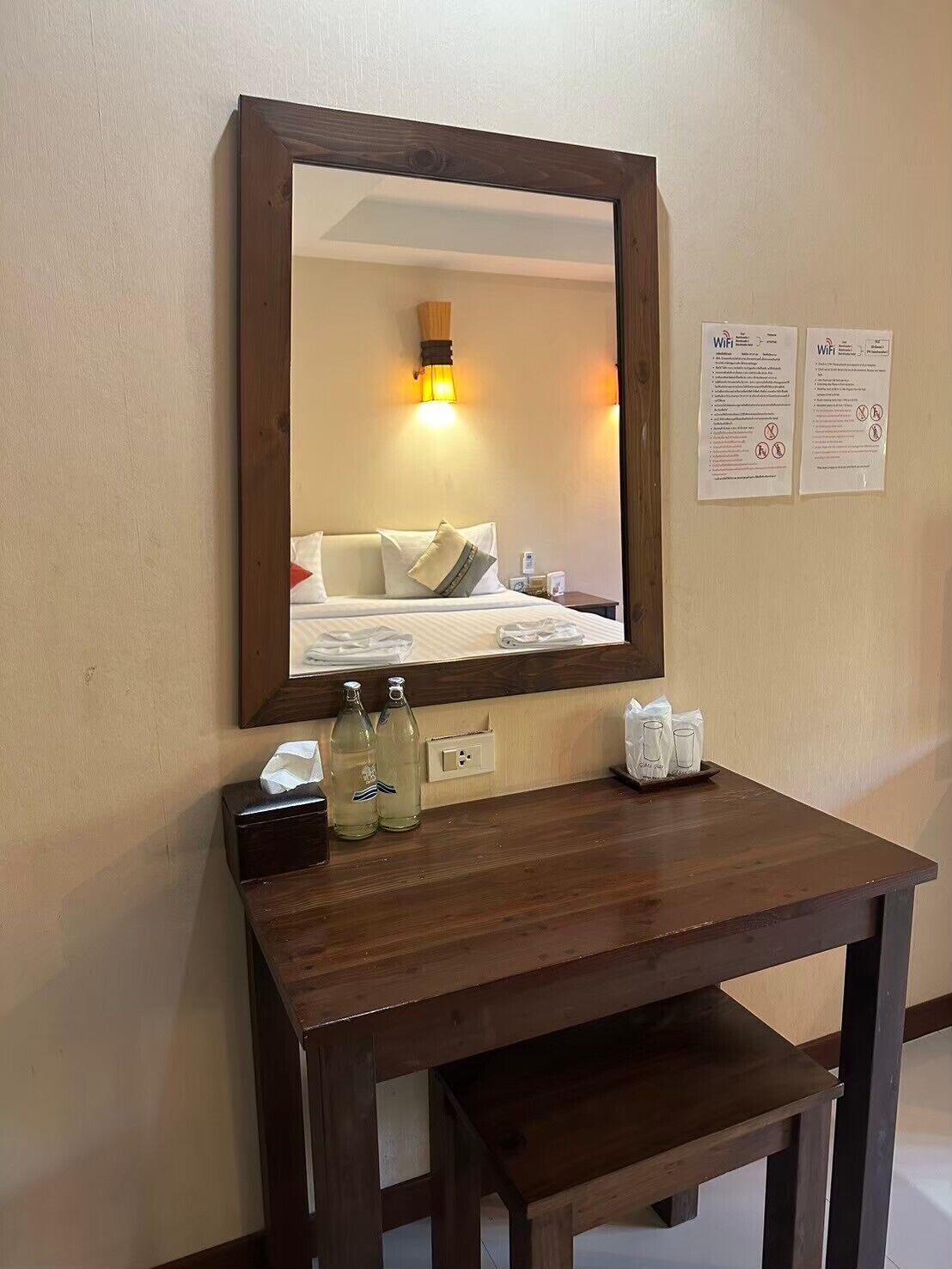 Habitación de hotel con un escritorio de madera, un espejo y dos carteles informativos en la pared.