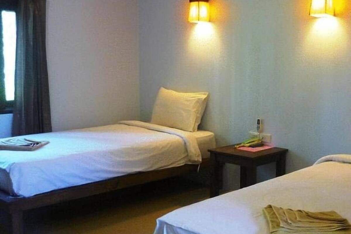 A single bed with a white sheet, a bedside table with a lamp, and a window with curtains.