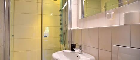 Une salle de bain moderne avec une douche à l’italienne en verre, un lavabo blanc et un miroir au-dessus.