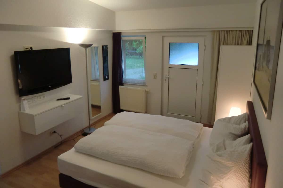 A hotel room with a bed, a TV, a desk, a mirror, a door, and a window.